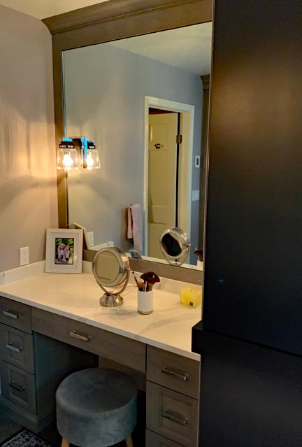 The make up area is a large vanity built in to the corner of the bathroom. There is a large mirror that extends to the ceiling. Underneath the vanity there are stacked drawers but there is also space in the middle where a stool sits.